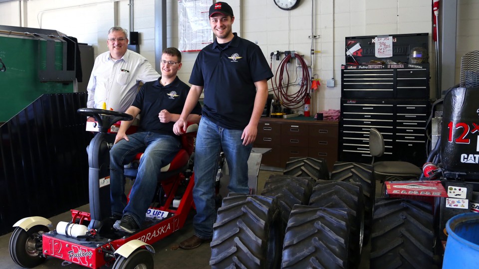 Roger Hoy (from left), Caleb Lindhorst and Luke Prosser show off a tractor designed by students for a 2014 engineering competition. Lindhorst was involved in a December 2013 auto accident and support from Hoy and Prosser has helped him return to classes o