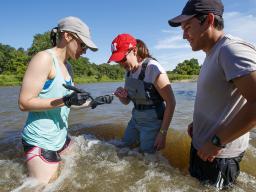 From left to right, Kayla Vondracek, Jessica Corman and Matthew Chen take a look at an algae sample while standing in the Niobrara River.
