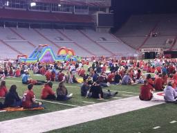 Students and family members watch a football game on the big screen in Memorial Stadium.