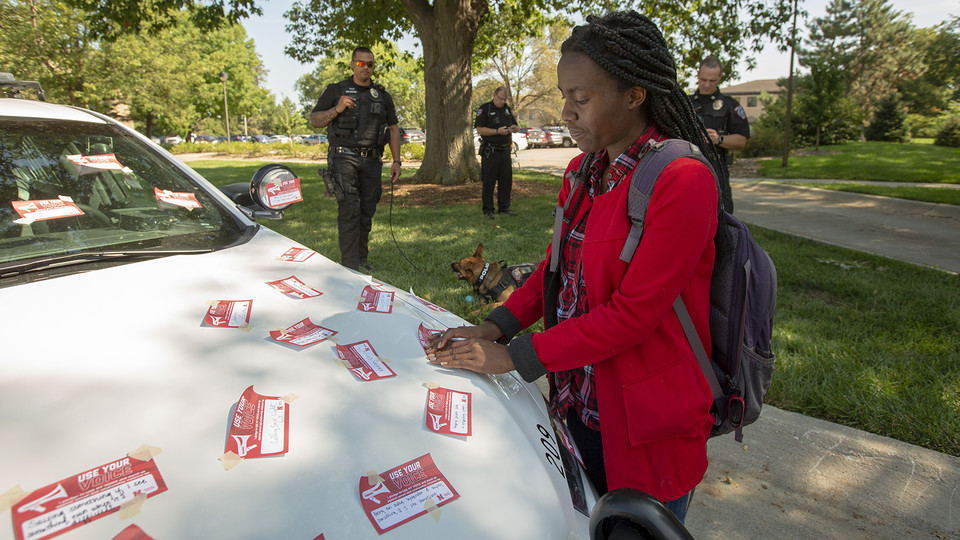 Elizabeth Uwase, a junior integrated science major from Rwanda, affixes her "Use Your Voice" pledge to a police car during the Sept 10 Cover the Cruiser event on East Campus. | Troy Fedderson, University Communications