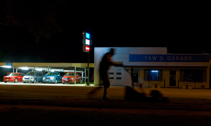 A man mows the lawn across the street from Faw's Garage in Arapahoe, Neb., in this photo from the "Real Nebraska" series.