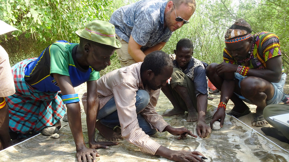 Matthew Douglass, assistant professor of practice in the College of Agricultural Sciences and Natural Resources, (standing) works with Daasanach men to mark out pasture boundaries, watering points and conflict areas on prints of satellite imagery. | Court