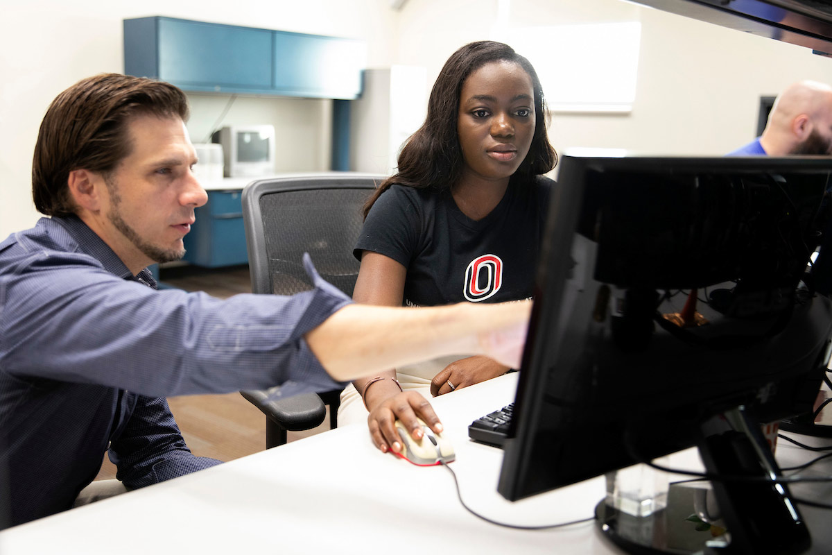 Student looking at a computer with a teacher pointing to something on the screen.