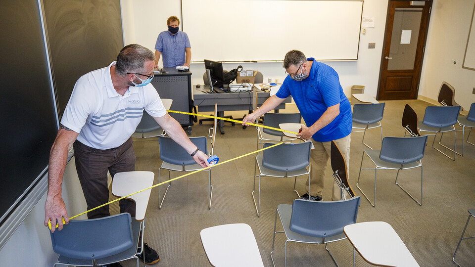 Jack Dohrman (left) and and Shawn Languis (right), use tape measures to gauge physical distancing needs within an Avery Hall classroom. Keith Derickson, a support manager with academic technologies, stands in the instructor position to assist with the map