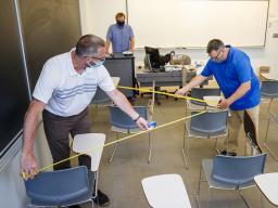 Jack Dohrman (left) and and Shawn Languis (right), use tape measures to gauge physical distancing needs within an Avery Hall classroom. Keith Derickson, a support manager with academic technologies, stands in the instructor position to assist with the map