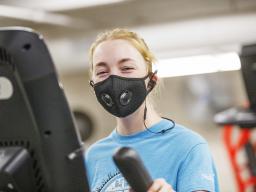 A student wears a black face covering while exercising in the Campus Rec Center's strength training & conditioning room.