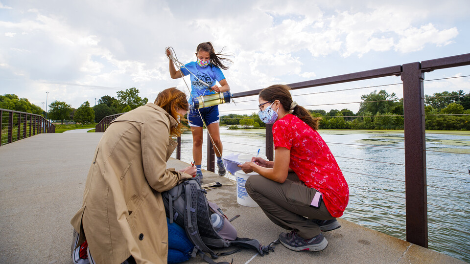 Malayna Wingert lifts a water sample out of Holmes Lake as Anni Poetz and Maddie Carpenter record data in August 2020. 