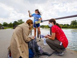 Malayna Wingert lifts a water sample out of Holmes Lake as Anni Poetz and Maddie Carpenter record data in August 2020. 