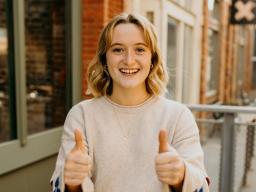 Clare Frances Kennedy smiles and holds two thumbs up