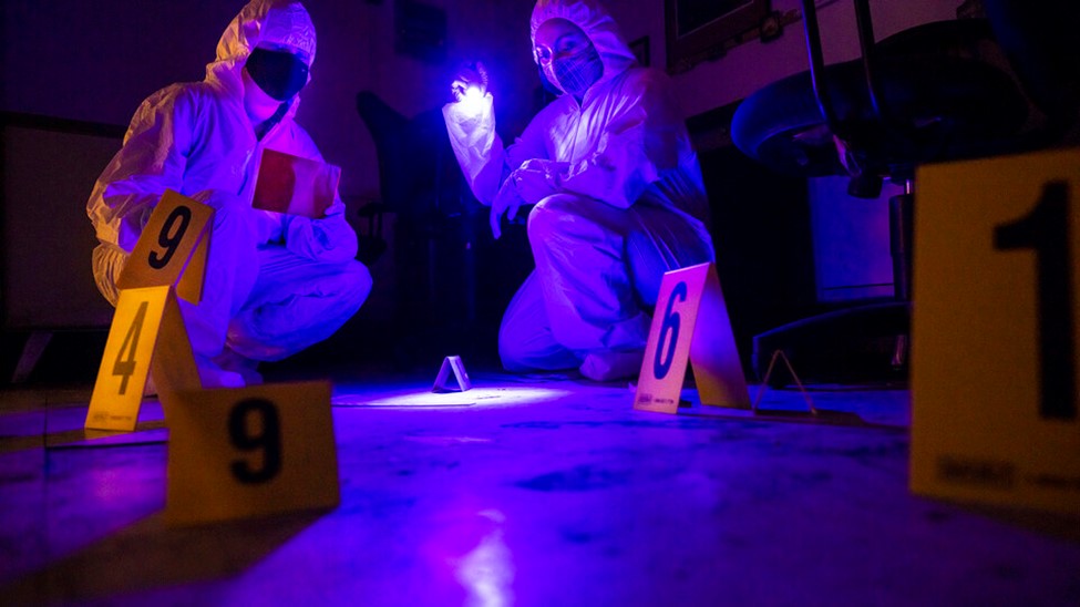 Symone Arends, a senior from Lincoln, shines an ultraviolet light onto the floor. The light makes body fluids and fibers glow when viewed through the filter held by Alysa Ehlers, a senior from Woodbridge, Virginia. The two are working a mock crime scene i