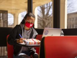 Gabriella Silva (red mask) and Zoe Keese (white mask) study at the tables in the sun lit lobby inside Hamilton Hall during the spring 2021 semester.