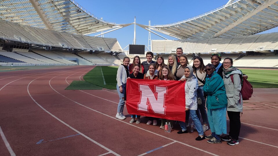 Twelve students, led by faculty members Georgia Jones and Dennis Perkey, pose with a Husker flag in the 2004 Olympic stadium. Courtesy Dennis Perkey.