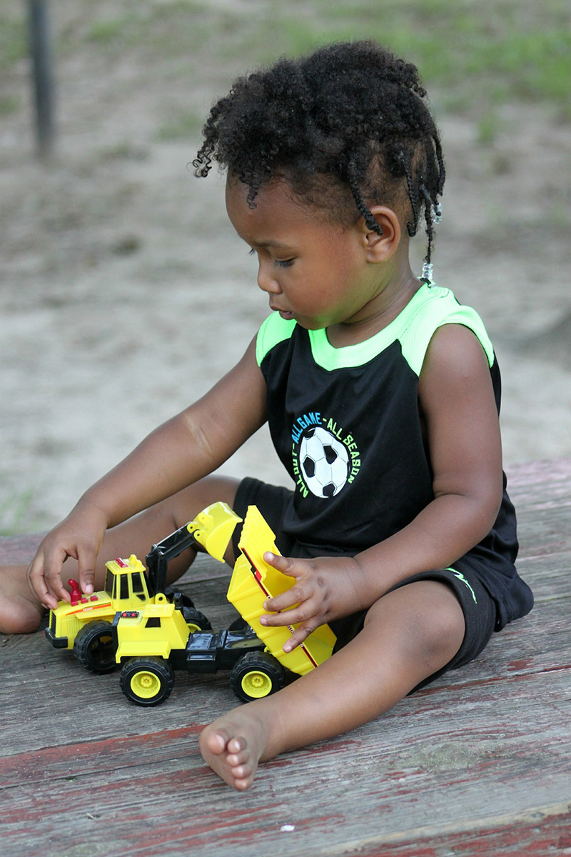 Little boy playing with trucks while sitting on a picnic table.