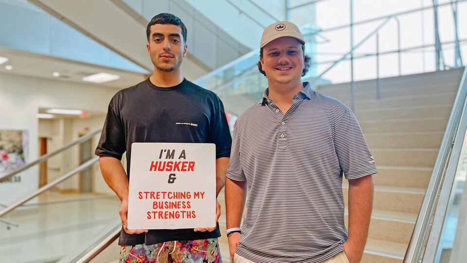 Rob Khorrom and Zach Molzer smile for a photo inside Hawks Hall with a sign that reads “I’m a Husker & stretching my business strengths."