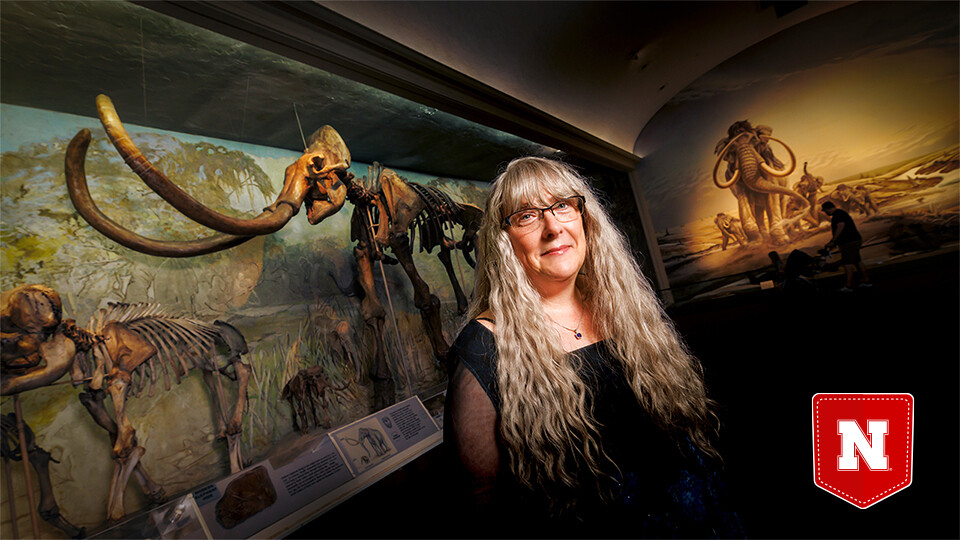  Nebraska’s Kate Lyons stands in Elephant Hall at the University of Nebraska State Museum. Behind her looms Archie, the largest Columbian mammoth fossil in the world. Craig Chandler | UComm