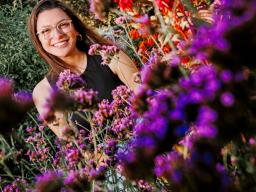 Isabella Villanueva smiles for a photo surrounded by flowers on East Campus. 