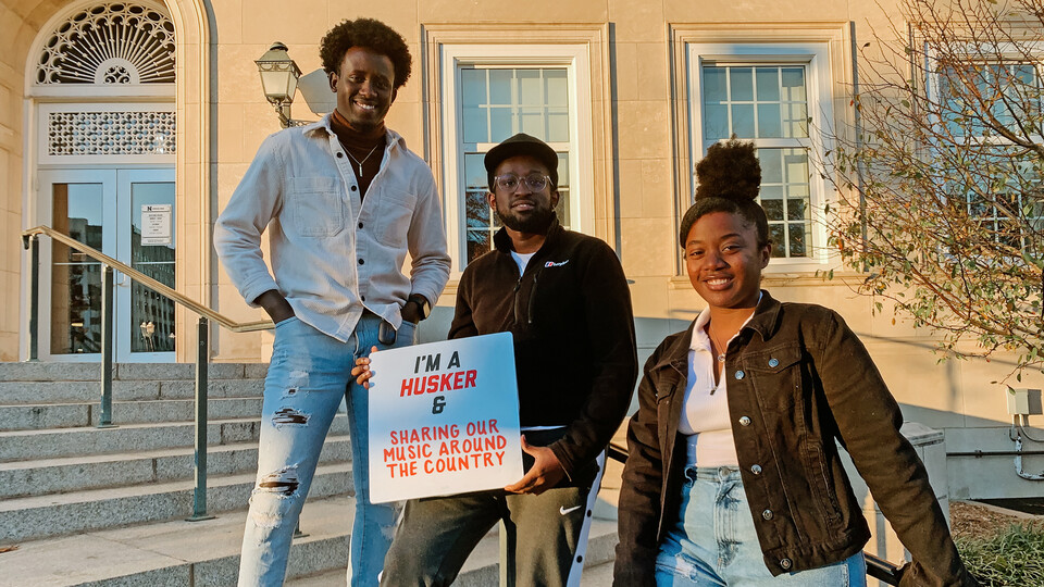 Live Lyve members (from left) Japhet Ingeri, Benoit Kayigamba and Esther Uwamahoro pose in front of the Union. Kayigamba holds a sign that reads "I'm a Husker & Sharing Our Music Around the Country."
