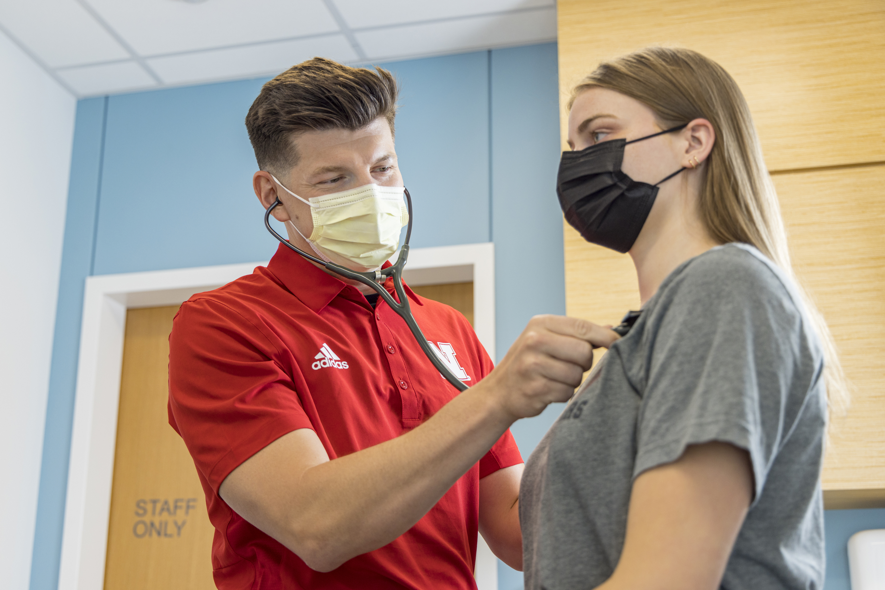 Doctor using a stethoscope to check a student's heart.