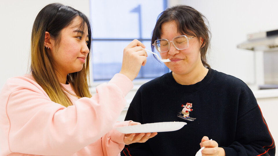 Zhuo Chen wrinkles her nose after smelling a cheese sample held by Baoyue Zhang.