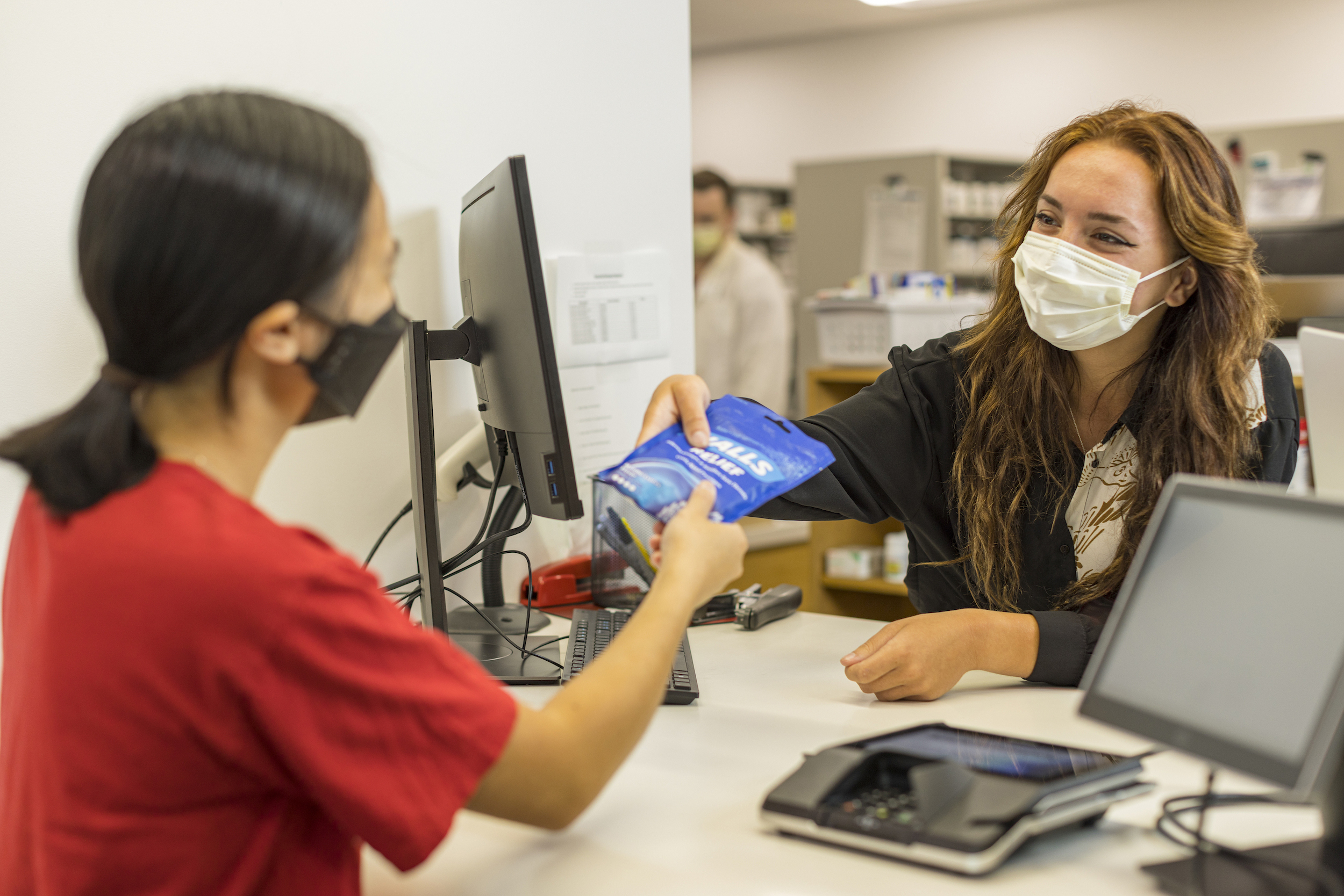 Pharmacist handing a bag of cough drops to a student.