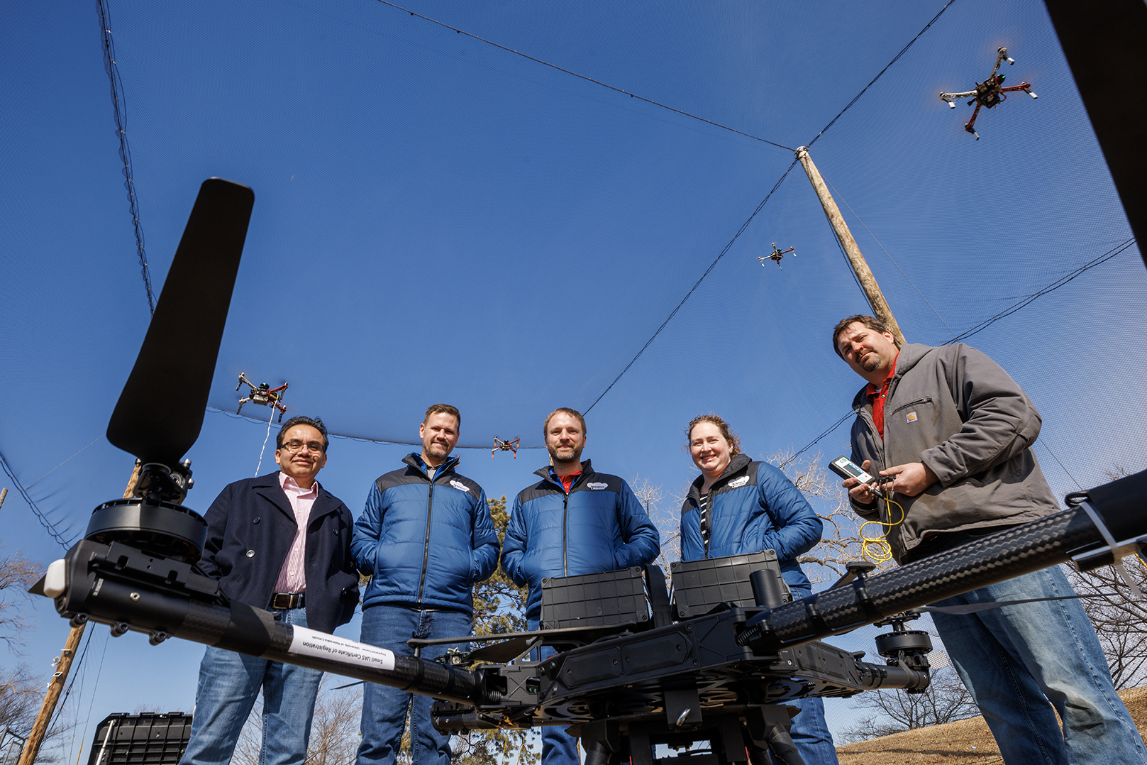 (From left) Francisco Muñoz-Arriola, Justin Bradley, Carrick Detweiler, Brittany Duncan and Trenton Franz pose among unmanned aerial vehicles at the NIMBUS outdoor flying area on Nebraska Innovation Campus.