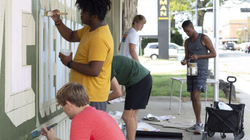 Students from Sandra Williams’ University Honors seminar help Shawn Dunwoody (right) paint his mural at the Veterans of Foreign Wars. | Photo by Eddy Aldana.