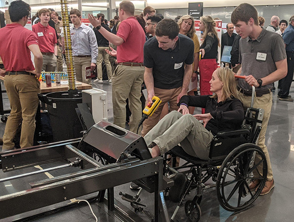 Mechanical engineering students James Admiraal and Levi Schulze demonstrate their project, "Pneumatic Leg Press for MS Patients," to a visitor during the 2024 college's Senior Design Showcase May 3 at Kiewit Hall.