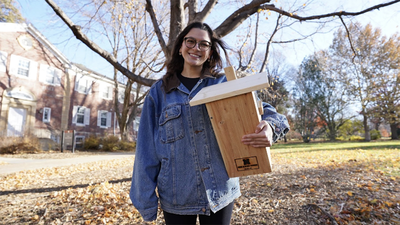 Isabella Villanueva, a senior UNL fisheries and wildlife major, stands with a flying squirrel nesting box near Hardin Hall on East Campus.