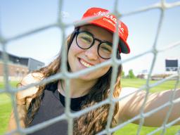 Cece Villa, Husker soccer goalkeeper, smiles for a photo through the net of the goal.