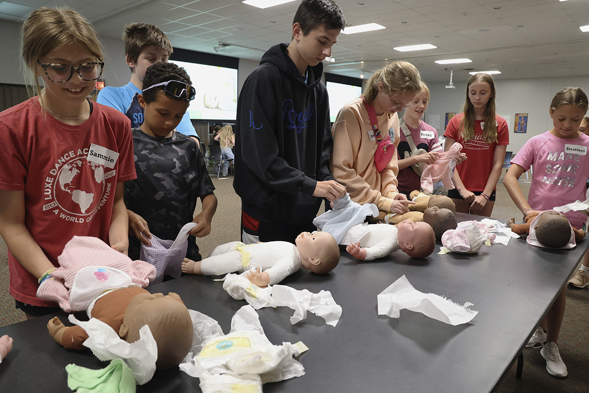 eight youth practicing changing diapers on realistic dolls