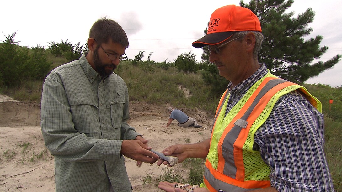 Carl Hart, Nebraska Department of Transportation project manager, gives several bones that he recovered on a project in north central Nebraska to Shane Tucker, highway paleontologist. Photo courtesy Nebraska Public Media