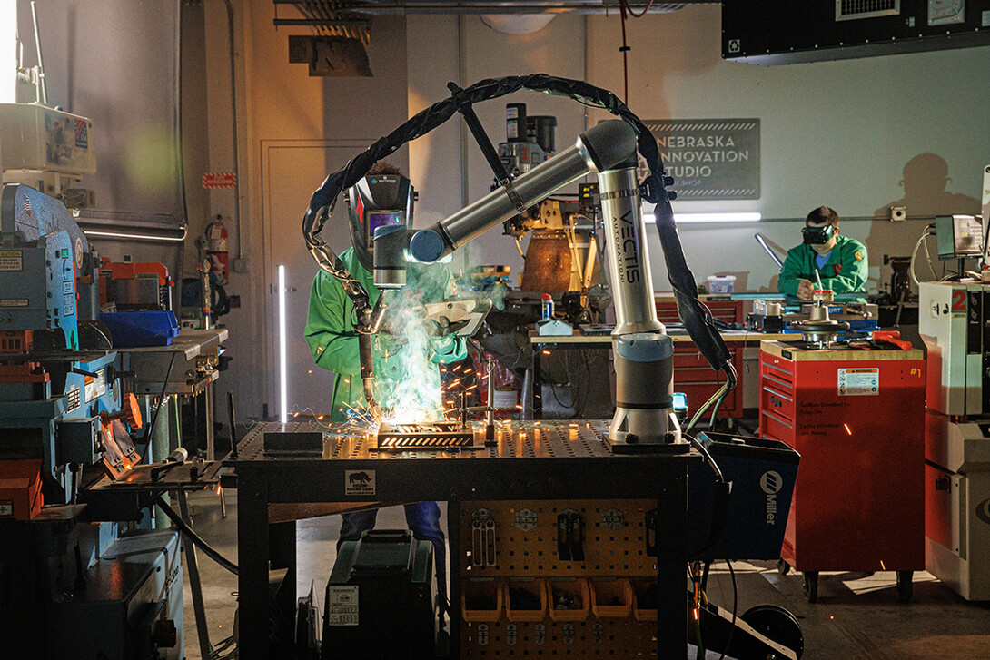 Kristen Labadie | A Nebraska Innovation Studio member watches the welding robot while checking the programming on a tablet.