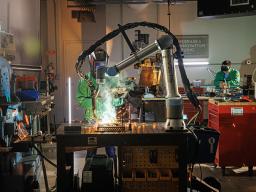 Kristen Labadie | A Nebraska Innovation Studio member watches the welding robot while checking the programming on a tablet.