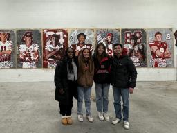 Left to right:  Michelle Reese, Maddie Vanderbur, Lea Bushey and Micah Fullinfaw stand in front of the mural they created to spotlight the players signed on National Signing Day by the Nebraska Football team. Courtesy photo.