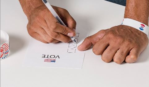 Two hands with the left holding a pen and marking an X in a box