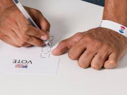 Two hands with the left holding a pen and marking an X in a box