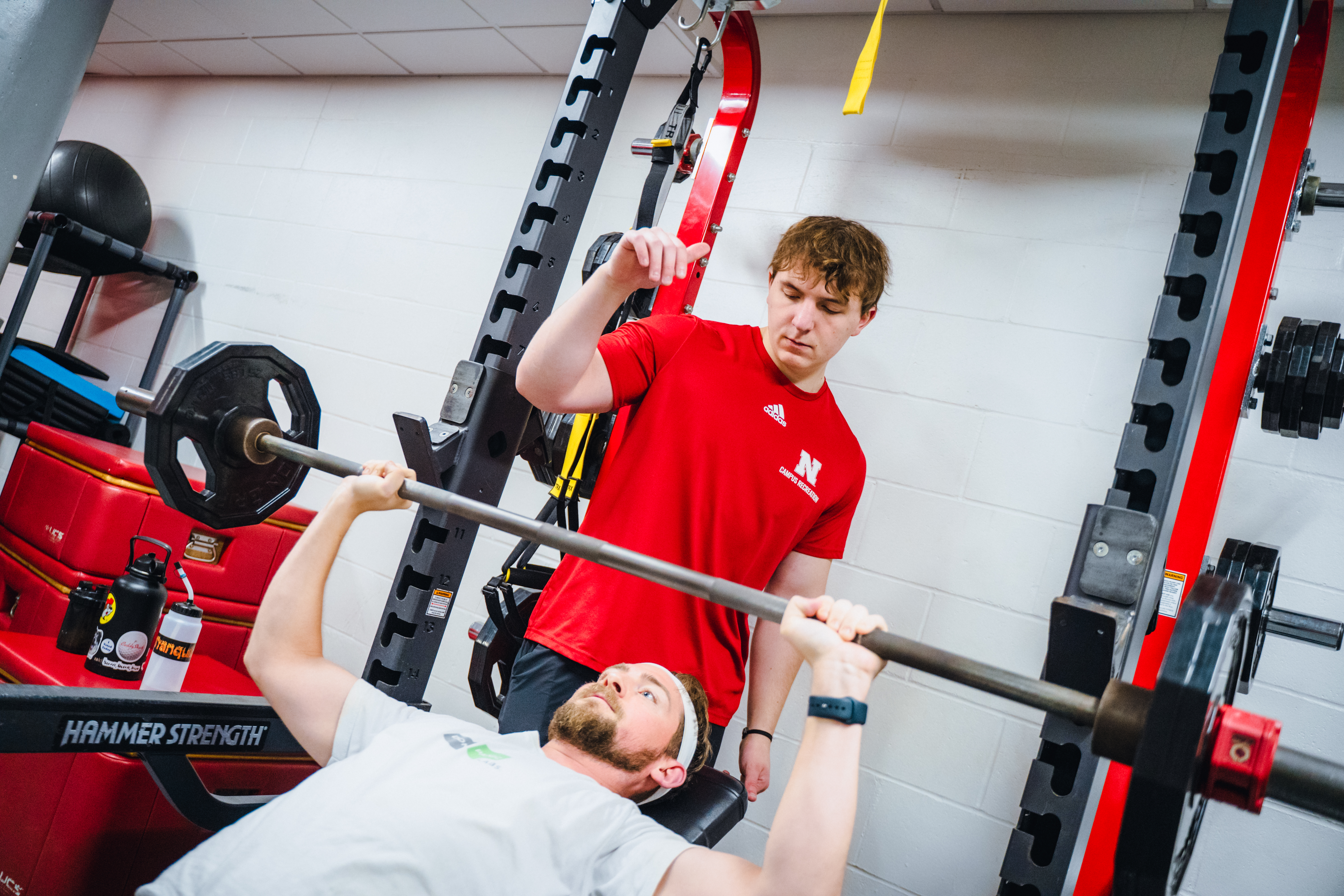 A personal trainer stands behind their client to spot them while they do a bench press.