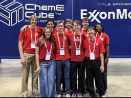 Top left photo: The UNL ChemE Cube Team; Bottom left photo: Team receiving feedback after poster presentation; Top right photo: Side profile of the cube; Bottom right photo: The cube in action during the Run segment of the competition.