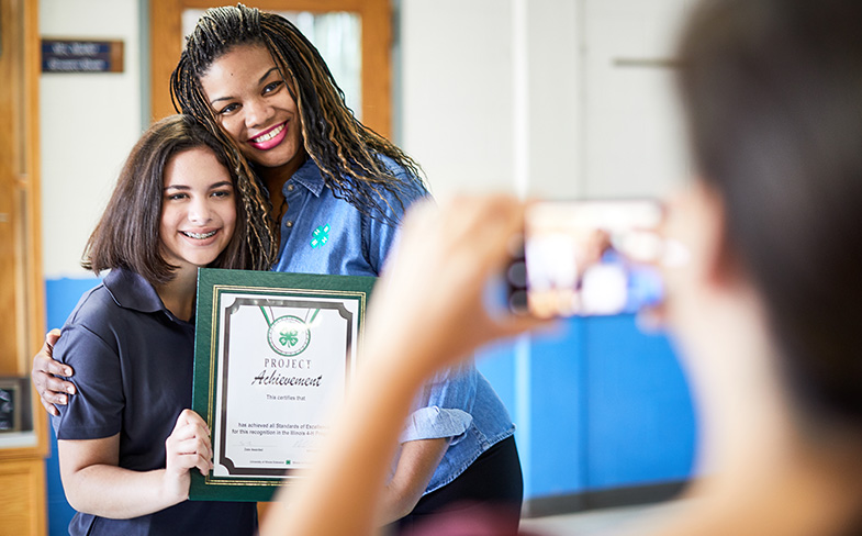 4-H leader and youth participant smiling for photo with certificate