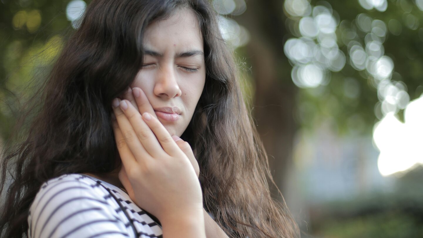 Person, in pain, holding one side of their cheek with both hands