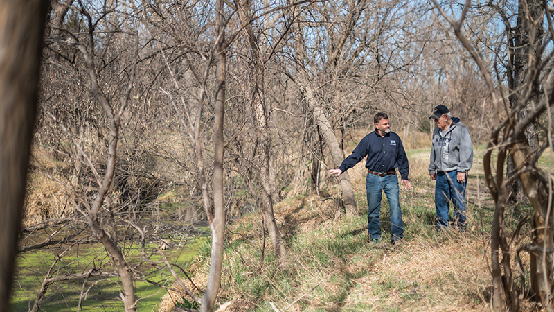 Ryan Powers, 1996 alumnus of the School of Natural Resources, speaks to a landowner about options for managing damage from beavers backing up water on his property and girdling his trees with it.