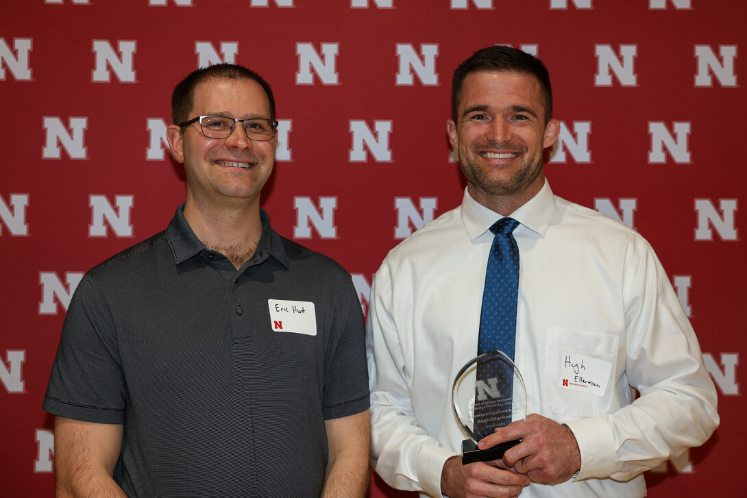 Ellerman (at right) receives a trophy after Eric Hunt (on left) announces he won the 2026 Postdoctoral Excellence Award. Photo by Marissa Lindemann