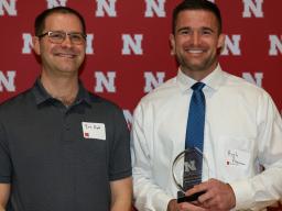 Ellerman (at right) receives a trophy after Eric Hunt (on left) announces he won the 2026 Postdoctoral Excellence Award. Photo by  Marissa Lindemann 