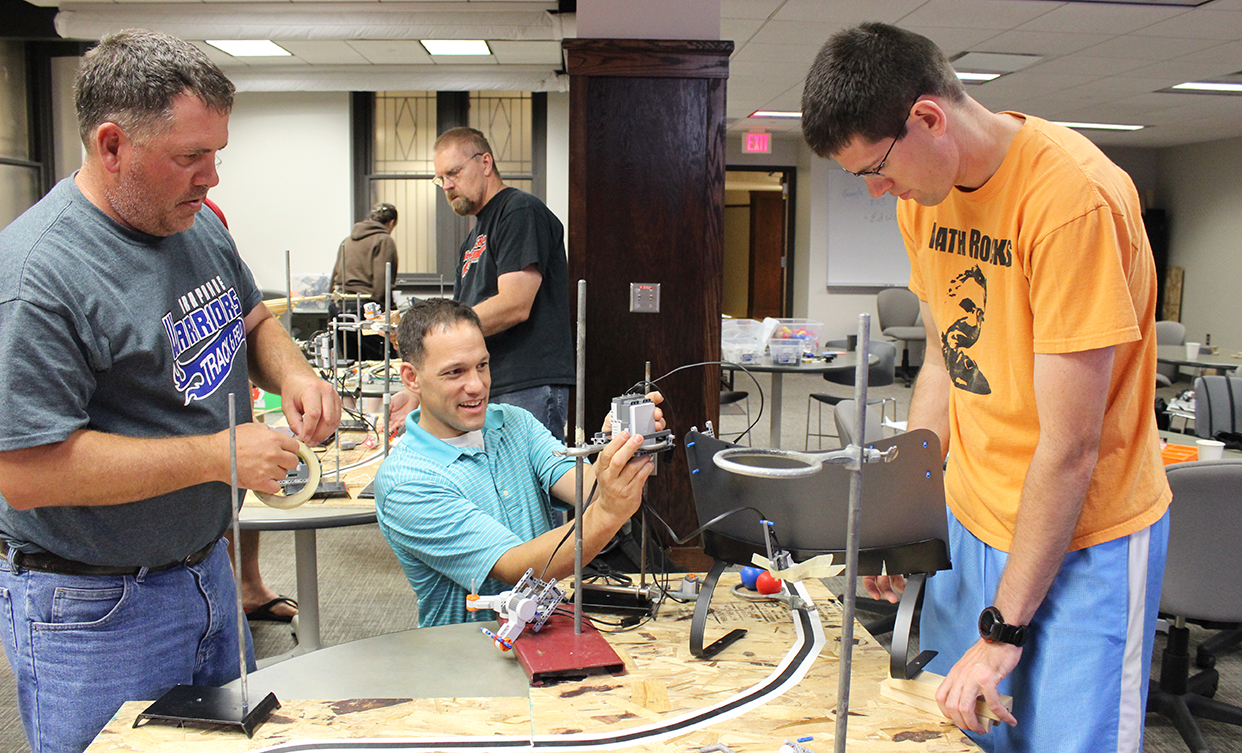 Jesse Andres (center), instructor for CSCE 890: Robotics for Teachers, helps Dan Schaben (left) and Matt James set up their robots.
