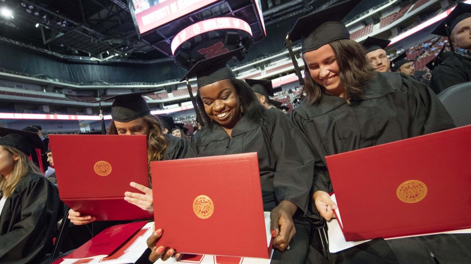 (From left) Julia Storm, Davetta Nelson and Gianna Astorino look over their diplomas in criminal justice during the all-university commencement ceremony Aug. 13 at Pinnacle Bank Arena. | Craig Chandler, University Communications 