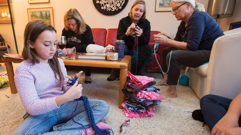 Nylah Mossop (left) uses her fingers to knit a scarf during the launch of the "Scarves for Kids" project on Nov. 20. The event was organized by Jo Ann Emerson (right) and Sandra Williams (not pictured). Other participants included (left of Emerson) Amanda