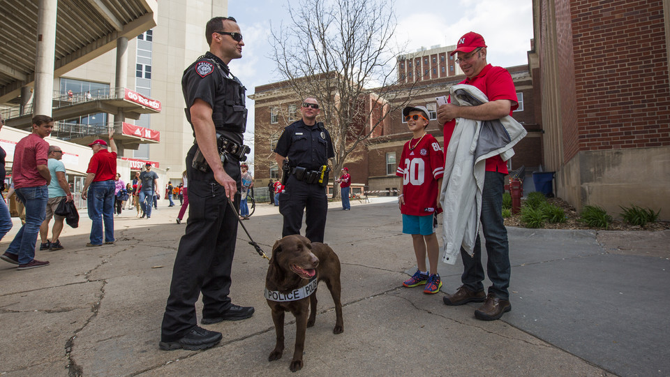 Troy Fedderson | University Communication | K-9 handler Greg Byelick (left) discusses his new partner, Justice, with Mike Heller (right) and his son Robbie prior to the start of the Huskers' spring football game on April 15.