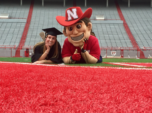 Abby Akin (left) celebrates graduation on August 14, 2017 with Nebraska Mascot Herbie Husker in Memorial Stadium. (Photo/Kyra Willats)