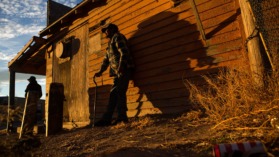 People stand beside a building as the sun sets over Whiteclay. Many of those who spend time drinking on the streets in Whiteclay spend their nights in a makeshift camp not far from the town.