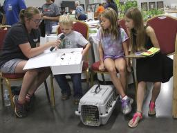 Many 4-H Clover Kids (ages 5–7) who entered static exhibits also participated  in Show & Tell. Clover Kid activities are non-competitive, and they receive  rainbow participation ribbons. Pictured is a youth talking about his insect collection box.